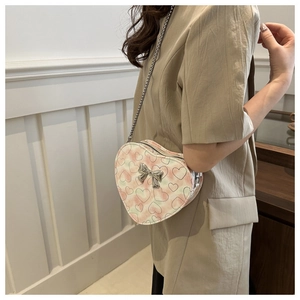 Detail of a heart-shaped crossbody bag with tie-dye print and silver bow accent