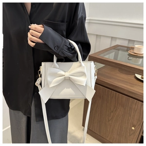 Close-up of elegant white handbag with large decorative bow on a wooden surface