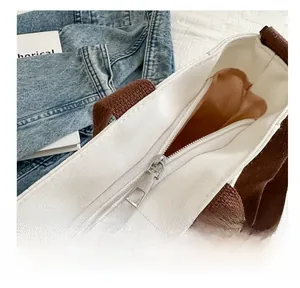 Close-up of smooth silver metal zipper and brown woven handles on a white canvas tote bag