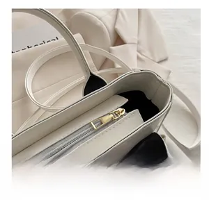 Detail view of the smooth golden zipper and premium white leather texture on the tote bag