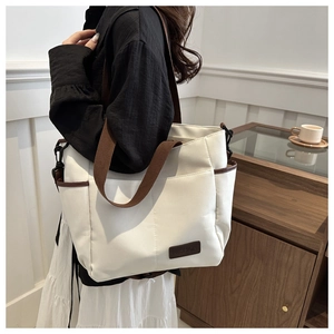Close-up of white canvas tote bag with brown straps and fashion leather logo patch