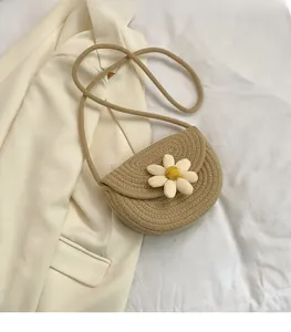 Close-up of khaki crochet crossbody bag with a white 3D daisy flower on white fabric