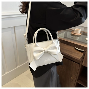 Close-up of structured white PU handbag with a large bow detail and thin shoulder strap