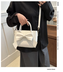 Detail shot of white crossbody bag with large bow and golden metal buckle on strap