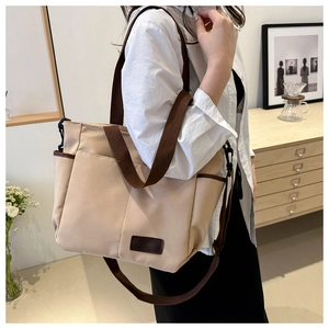Close-up of beige canvas tote bag with brown leather FASHION label and side pocket detail