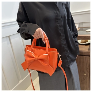 Detail of orange handbag featuring a large bow and adjustable shoulder strap