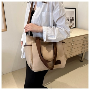 Detail of a large beige canvas tote bag with brown straps worn on a model's shoulder
