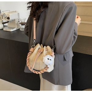 Detail of woven straw bucket bag with pink leather handle and plush ball charm decoration