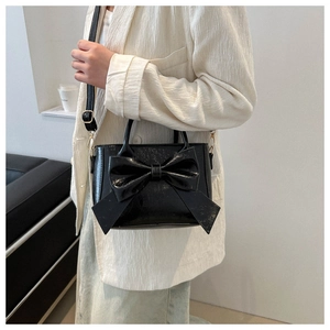 Black leather small square bag with large bow detail shown on a model's shoulder