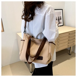 Detailed side view of a large beige canvas tote bag with brown straps on a person
