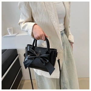Close-up of black glossy crossbody bag featuring a large bow and gold metal hardware
