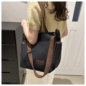 Detail of black canvas tote bag showing side pocket and adjustable brown shoulder strap