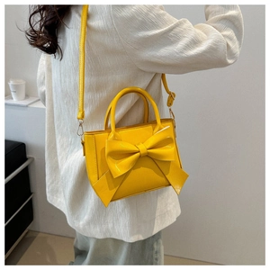 Detail of vibrant yellow bow handbag with glossy leather finish and shoulder strap