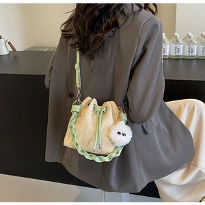 Detail of woven straw bucket bag with green leather drawstring and plush eye charm