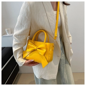 Macro detail of the yellow crossbody bag featuring a large bow and glossy patent finish