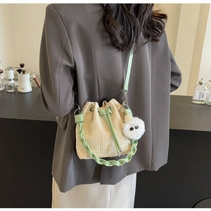 Detailed shot of straw bucket bag with green trim and a cute plush pompom accessory