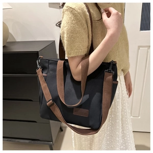 Close-up of black canvas tote bag showing dark brown nylon straps and side pocket detail
