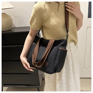 Detail of black canvas tote bag with brown leather straps shown on a model