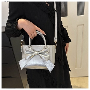 Detail of silver metallic handbag with large bow knot and textured finish on black dress