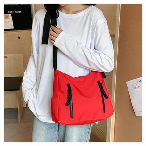 Détail d'un sac bandoulière rouge en nylon avec deux poches zippées et cordons noirs