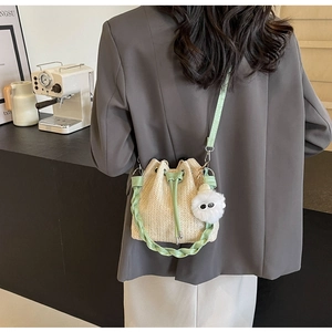 Close-up of beige woven bucket bag with green leather drawstring and decorative pom-pom