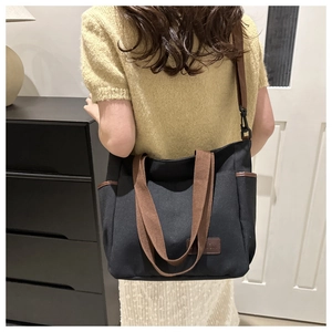 Detailed side view of large black canvas tote bag with adjustable brown shoulder strap