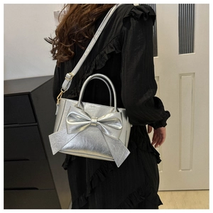 Silver bow shoulder bag shown on model with adjustable strap and metallic finish