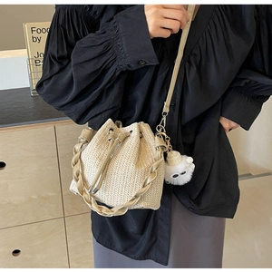Detail of beige woven bucket bag with drawstring closure and plush cat charm