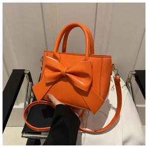 Detail of orange handbag featuring a large bow and metallic gold hardware details