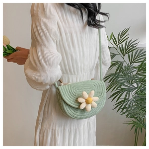 Detail of light green hand-woven saddle bag featuring a large white daisy flower decoration