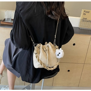 Detail of hand-woven straw bucket bag with drawstring closure and white fuzzy pom pom charm