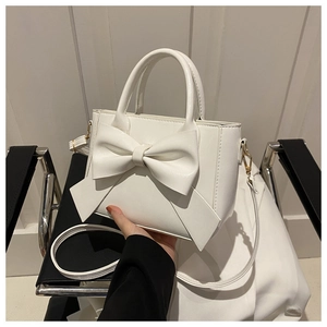 Detail of white PU leather mini bag with large bow and golden metal hardware on a chair