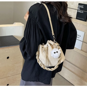 Detail of woven straw bucket bag featuring drawstring closure and fuzzy charm decoration