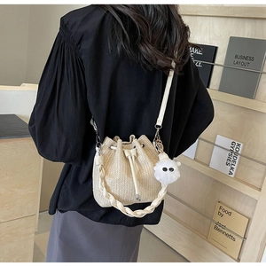 Detail of off-white woven bucket bag featuring drawstring closure and soft pompom charm
