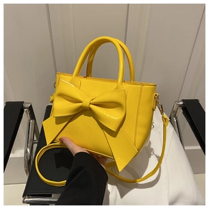 Detailed shot of yellow textured leather handbag featuring a large bow and top handles