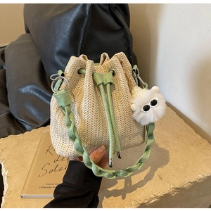 Detailed close-up of woven beige bucket bag with green leather trim and plush charm