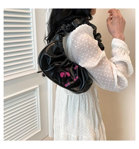 Detail view of black pleated cloud bag with pink butterfly embroidery on shoulder strap