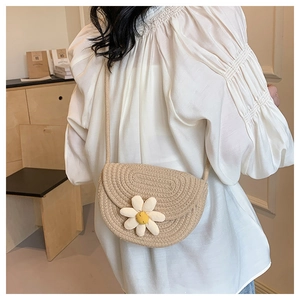 Close-up of beige woven crossbody bag with white daisy detail on model in white blouse