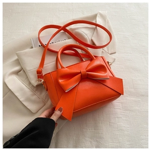 Detailed view of bright orange crossbody bag with large bow and PU leather texture