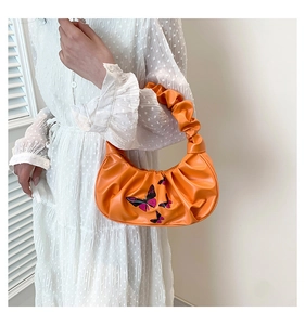 Detail of embroidered butterfly patterns on bright orange pleated cloud handbag