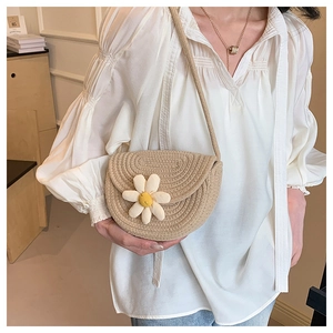 Close-up of khaki woven straw crossbody bag featuring a white daisy flower detail