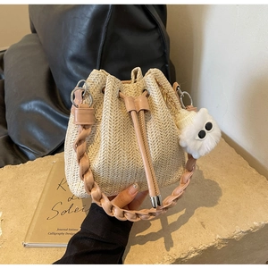Detail of cream woven bucket bag featuring pink faux leather trim and soft pom-pom charm