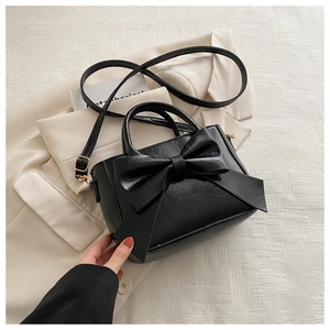 Close-up of black crossbody bag with large bow and gold hardware on beige blazer