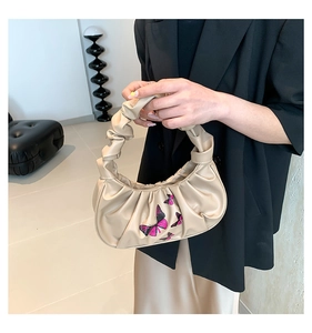 Detail of beige cloud bag with pink butterfly print held by a model in a black suit
