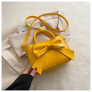 Close-up of bright yellow handbag with a large bow detail and gold metal hardware
