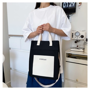 Detail of black and white canvas tote bag featuring JINNIAN lettering and shoulder strap