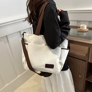 Minimalist white canvas tote bag with wide brown shoulder strap and fashion label