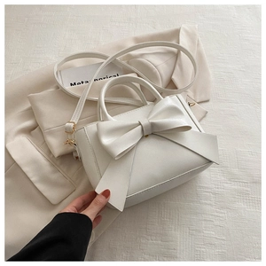 Detailed macro view of cream PU leather handbag with a large decorative bow and golden hardware