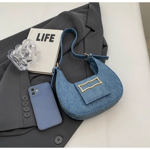 Detail of blue denim crescent bag with gold buckle on casual blazer background