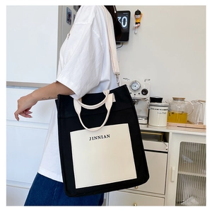 Detail of minimalist black canvas tote bag with white front pocket and JINNIAN logo